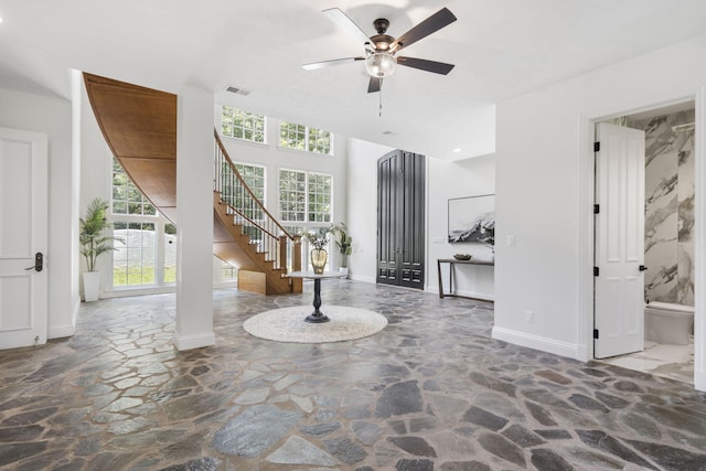 foyer entrance featuring stone flooring, a ceiling fan, stairs, and baseboards