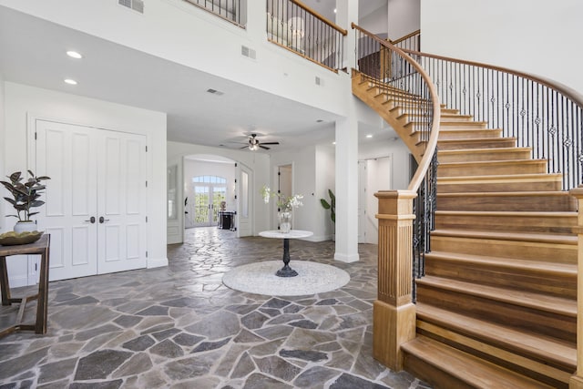 entrance foyer with stone flooring, arched walkways, stairway, baseboards, and a towering ceiling
