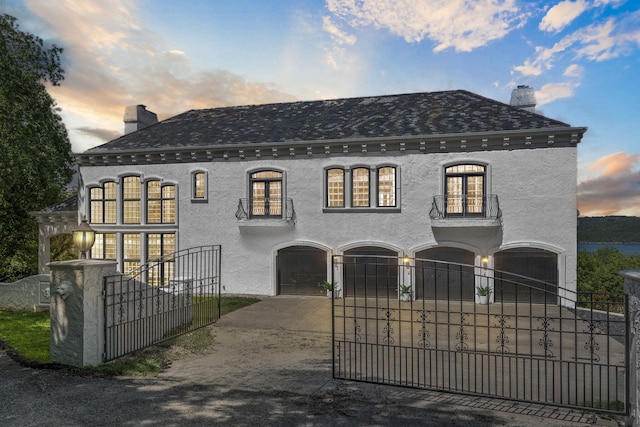 view of front of property with a garage, a balcony, concrete driveway, a chimney, and a fenced front yard