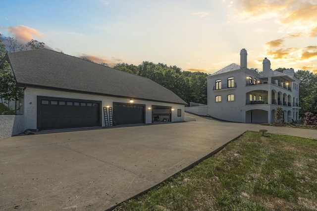 property exterior at dusk with driveway, a garage, stucco siding, and a chimney