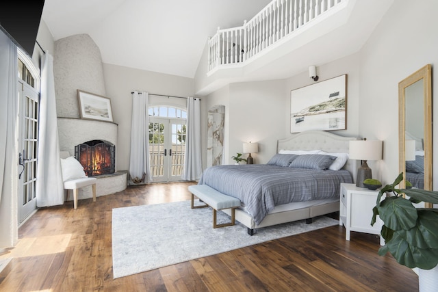 bedroom with french doors, high vaulted ceiling, wood finished floors, access to exterior, and a large fireplace