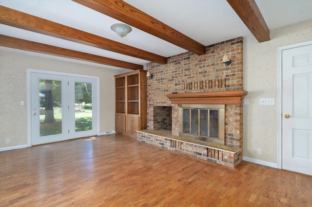 unfurnished living room with a brick fireplace, wood finished floors, baseboards, and beamed ceiling