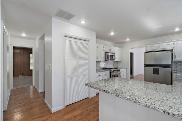 kitchen with stainless steel appliances, tasteful backsplash, dark wood finished floors, white cabinets, and a peninsula