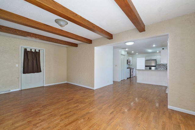 unfurnished living room with beamed ceiling, light wood-style floors, baseboards, and a textured wall