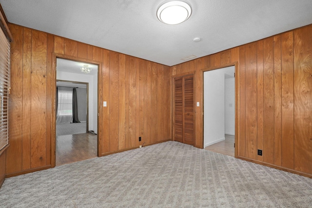 carpeted empty room with wooden walls and a textured ceiling