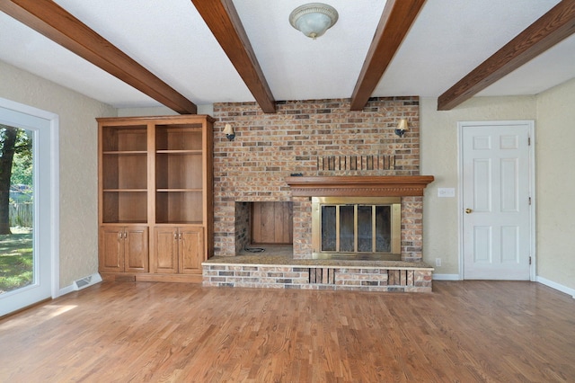 unfurnished living room with a brick fireplace, wood finished floors, baseboards, and beamed ceiling