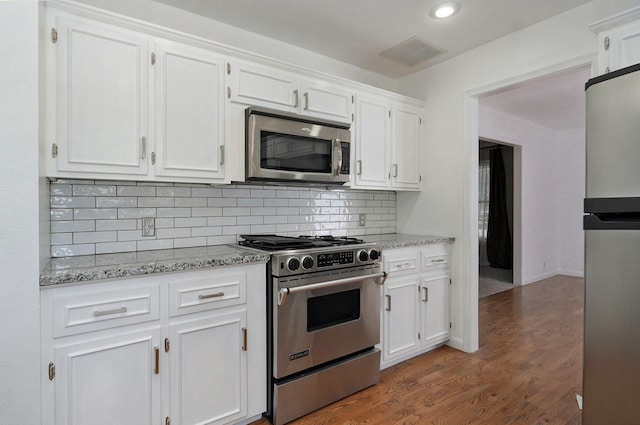 kitchen with appliances with stainless steel finishes, white cabinetry, light stone counters, backsplash, and dark wood-style flooring