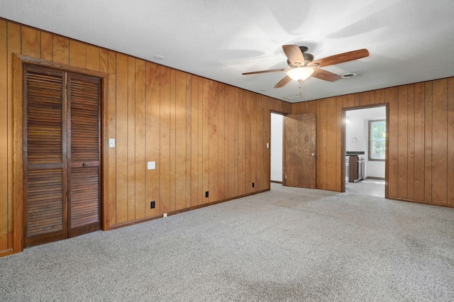 unfurnished bedroom featuring wooden walls, light carpet, connected bathroom, and a ceiling fan