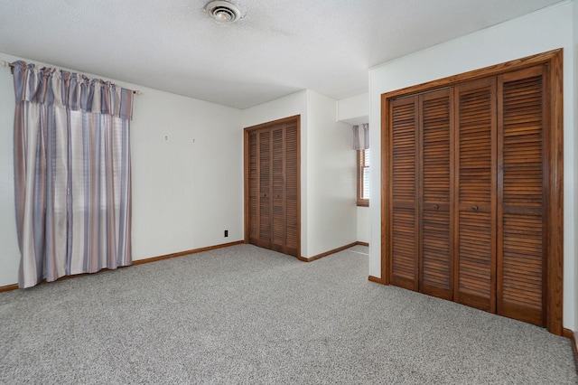 unfurnished bedroom with carpet floors, baseboards, two closets, and a textured ceiling