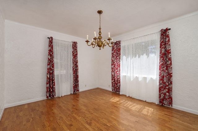 unfurnished room featuring a chandelier, wood finished floors, crown molding, and baseboards
