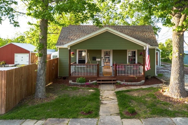 111 W Olive St, El Dorado Springs, MO 64744 - bungalow-style home with a shingled roof, fence, covered porch, an outbuilding, and a detached garage