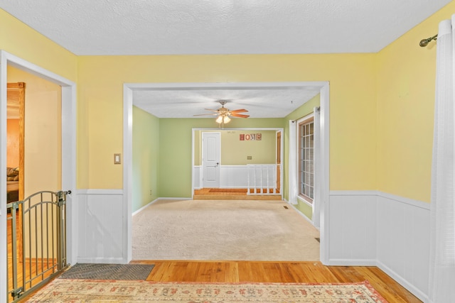 unfurnished room featuring wood finished floors, a wainscoted wall, ceiling fan, and a textured ceiling