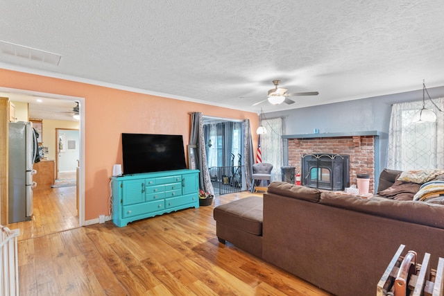 living area with a ceiling fan, light wood-type flooring, a textured ceiling, baseboards, and a fireplace
