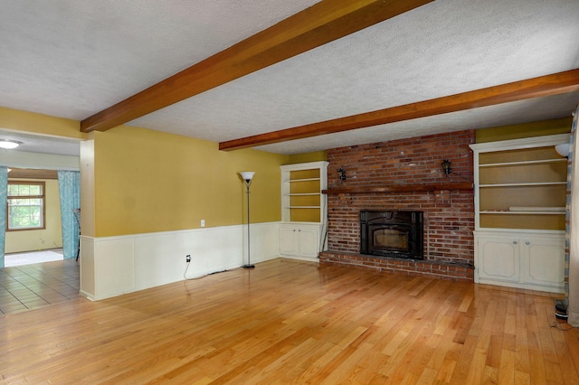4855 E Cimarron Ln, Springfield, MO 65803 - unfurnished living room featuring beam ceiling, wood finished floors, a fireplace, wainscoting, and a textured ceiling