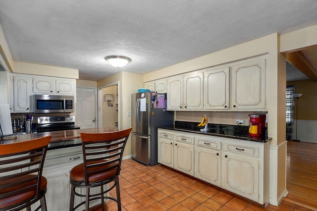 4855 E Cimarron Ln, Springfield, MO 65803 - kitchen with appliances with stainless steel finishes, dark countertops, a textured ceiling, light tile patterned floors, and baseboards