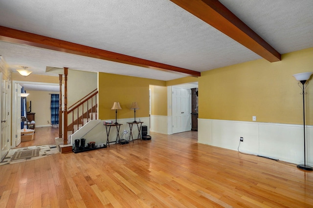 4855 E Cimarron Ln, Springfield, MO 65803 - unfurnished living room featuring beam ceiling, light wood-style flooring, stairs, a wainscoted wall, and a textured ceiling