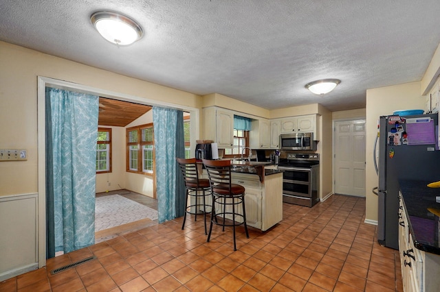 4855 E Cimarron Ln, Springfield, MO 65803 - kitchen featuring appliances with stainless steel finishes, a peninsula, dark countertops, a kitchen breakfast bar, and a textured ceiling