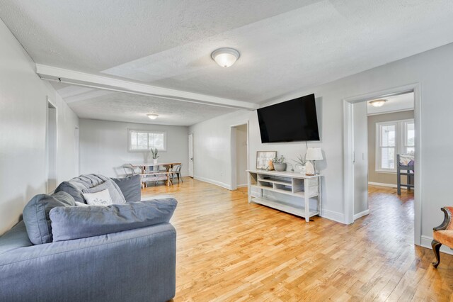 living area with a textured ceiling, light wood-type flooring, baseboards, and beam ceiling