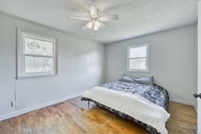 bedroom with wood-type flooring, baseboards, a textured ceiling, and ceiling fan