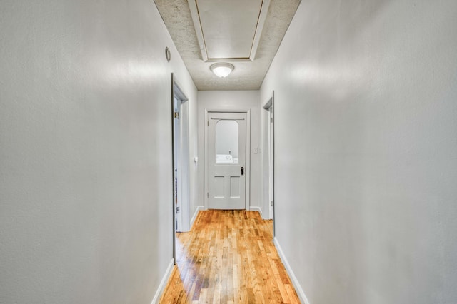 corridor with baseboards, light wood finished floors, and attic access