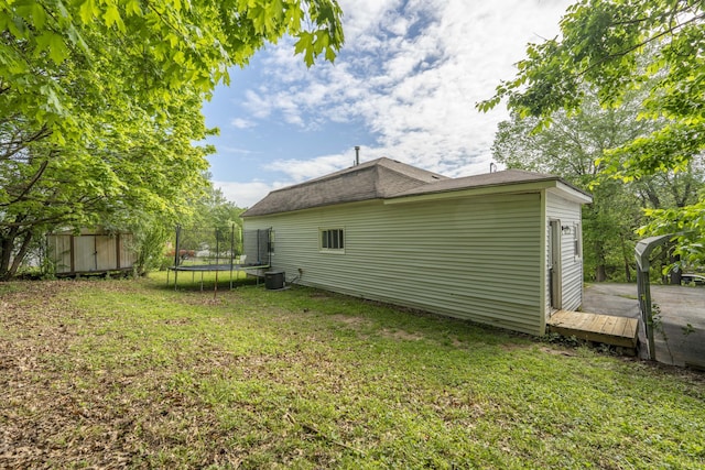 rear view of house featuring a trampoline, a lawn, a storage shed, an outbuilding, and a wooden deck