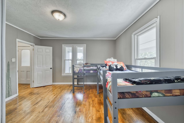 bedroom featuring ornamental molding, light wood-style flooring, multiple windows, a textured ceiling, and baseboards