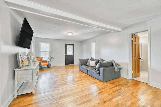 living room featuring a textured ceiling, light wood-style flooring, baseboards, and beamed ceiling