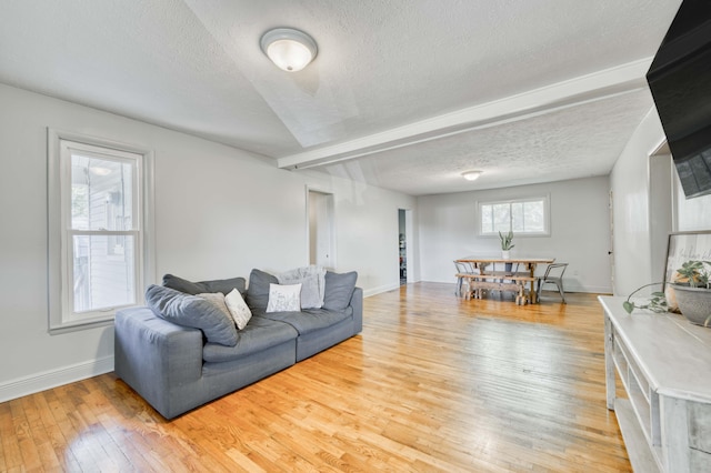 living area with baseboards, a textured ceiling, light wood finished floors, and beamed ceiling