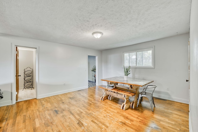 dining area with light wood-type flooring, baseboards, and a textured ceiling
