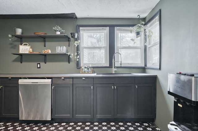 kitchen featuring stainless steel dishwasher, a sink, a textured ceiling, gray cabinets, and light countertops