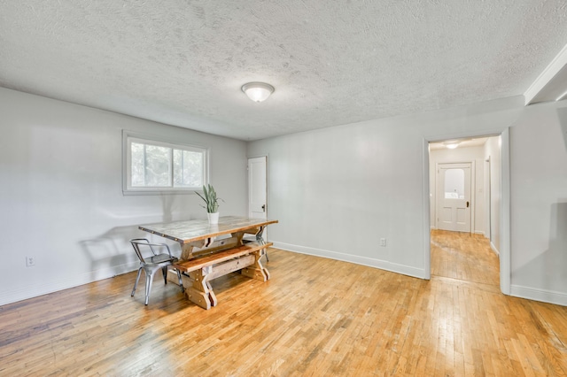 dining room with light wood-style floors, baseboards, and a textured ceiling