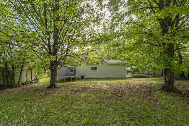 view of yard featuring a storage shed, an outbuilding, a trampoline, and fence