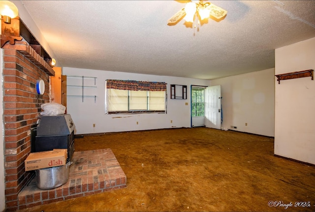 unfurnished living room featuring a wood stove, a textured ceiling, ceiling fan, and baseboards