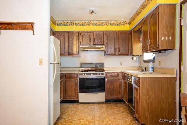 kitchen with range with gas stovetop, under cabinet range hood, freestanding refrigerator, light countertops, and a textured ceiling