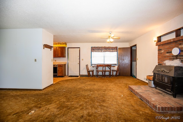 living area featuring a wood stove, carpet, a ceiling fan, and baseboards