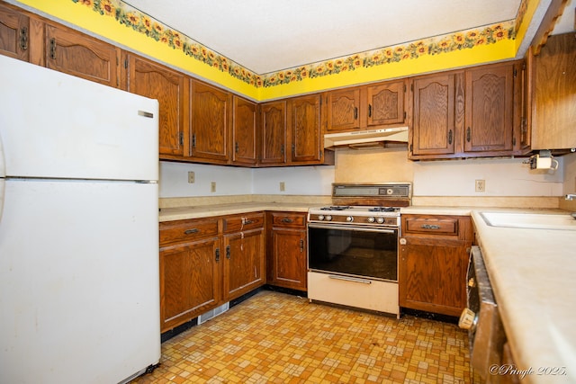 kitchen with white appliances, under cabinet range hood, a sink, light countertops, and brown cabinetry