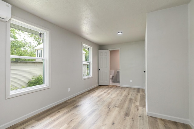 unfurnished room with a wall mounted AC, baseboards, light wood-type flooring, and recessed lighting