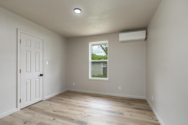 spare room with an AC wall unit, light wood finished floors, baseboards, and a textured ceiling