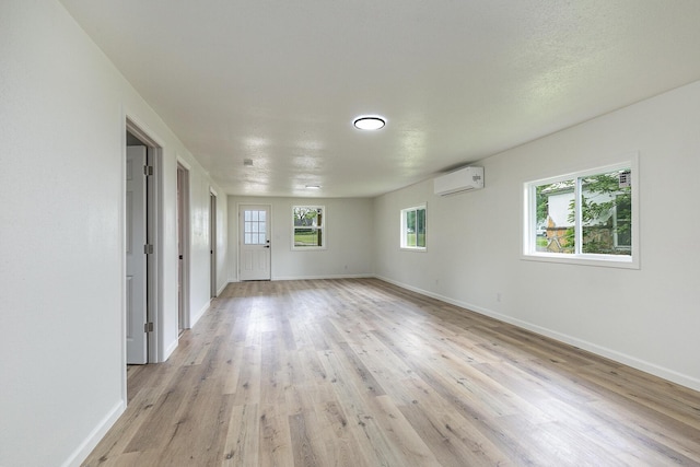 empty room with a wall unit AC, baseboards, and light wood-style floors