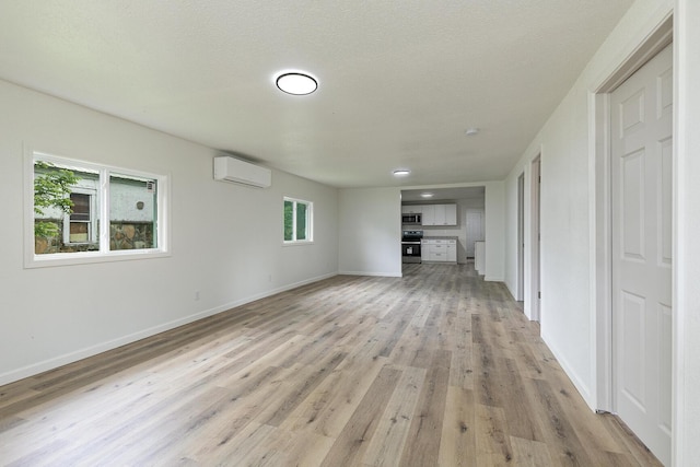unfurnished living room with a wall mounted air conditioner, light wood-type flooring, and baseboards