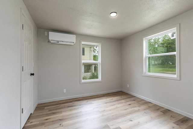 spare room with a wall unit AC, plenty of natural light, light wood-style floors, a textured ceiling, and baseboards