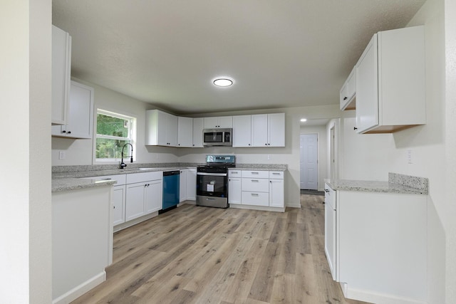 kitchen with stainless steel appliances, light wood-type flooring, white cabinets, a sink, and light stone counters