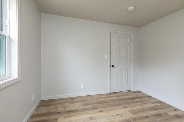 unfurnished room featuring light wood-type flooring, baseboards, and a smoke detector