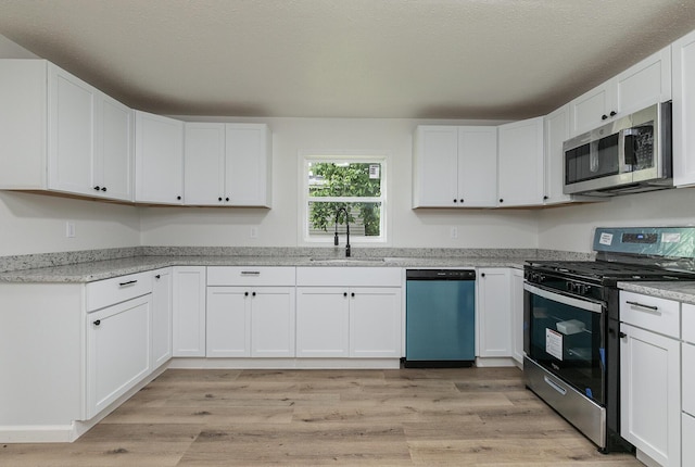 kitchen with stainless steel appliances, a sink, white cabinetry, and light wood-type flooring