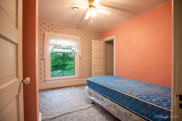 carpeted bedroom featuring a textured ceiling, ceiling fan, and wallpapered walls