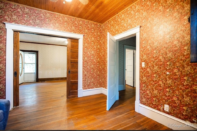 spare room featuring crown molding, wallpapered walls, wood finished floors, baseboards, and a ceiling fan