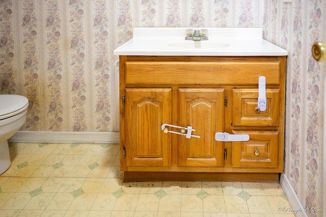 bathroom with baseboards, wallpapered walls, toilet, vanity, and tile patterned floors