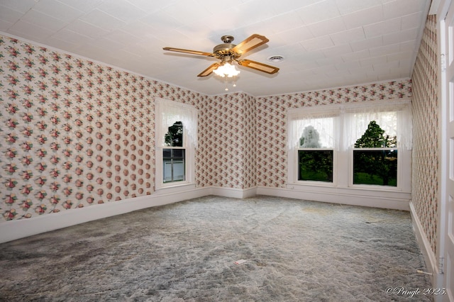 carpeted empty room featuring wallpapered walls, ornamental molding, a ceiling fan, and baseboards