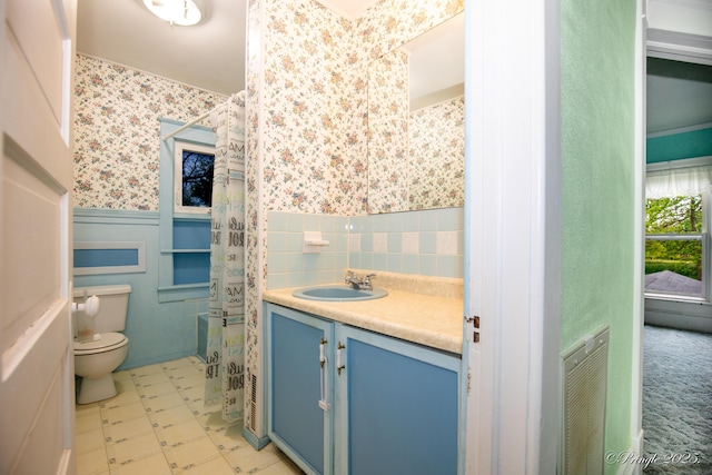 bathroom with toilet, wallpapered walls, a wainscoted wall, curtained shower, and vanity
