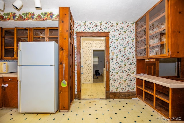 kitchen featuring white appliances, wallpapered walls, light flooring, glass insert cabinets, and light countertops